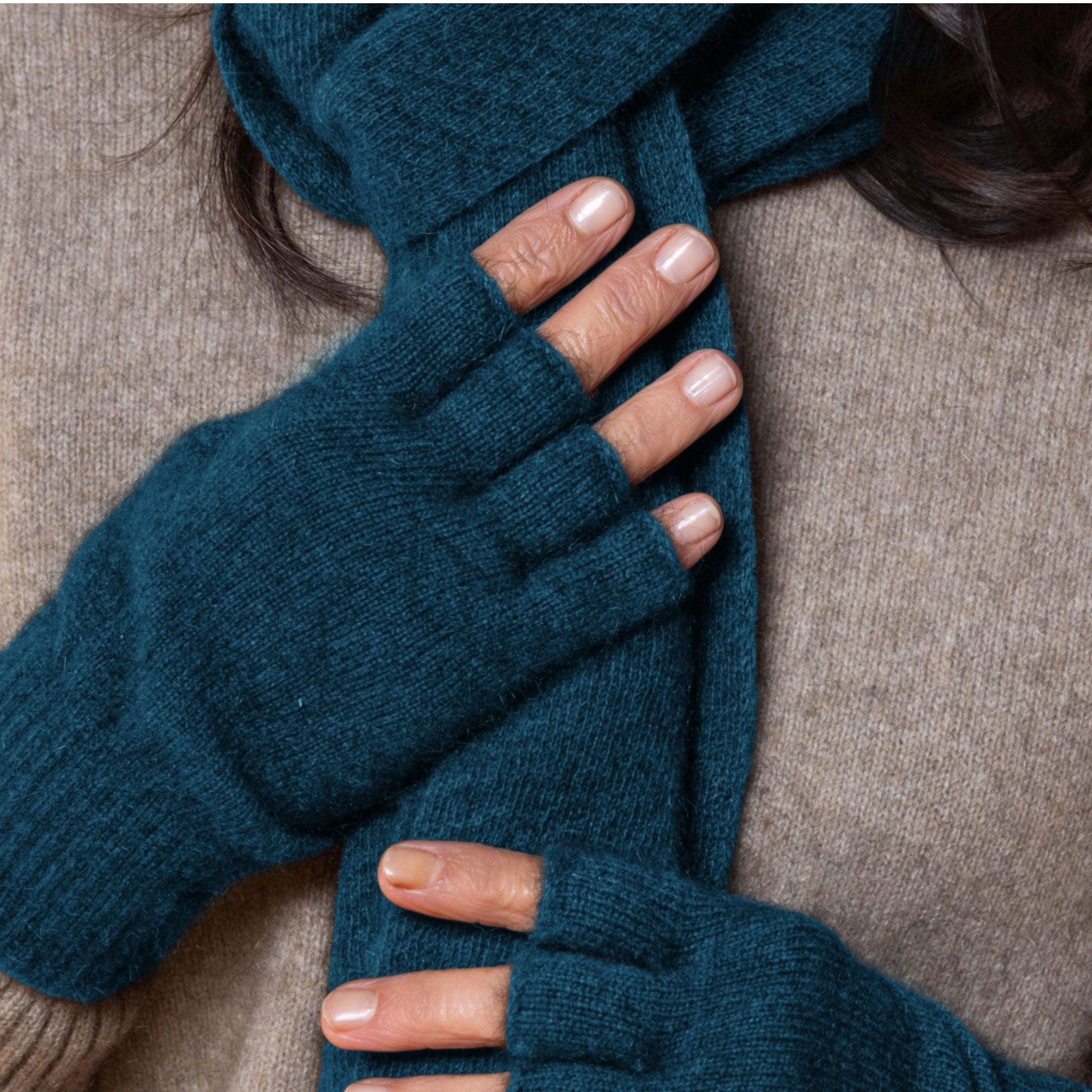 Close-up of a person wearing blue possum fingerless gloves and a matching scarf on a beige background
