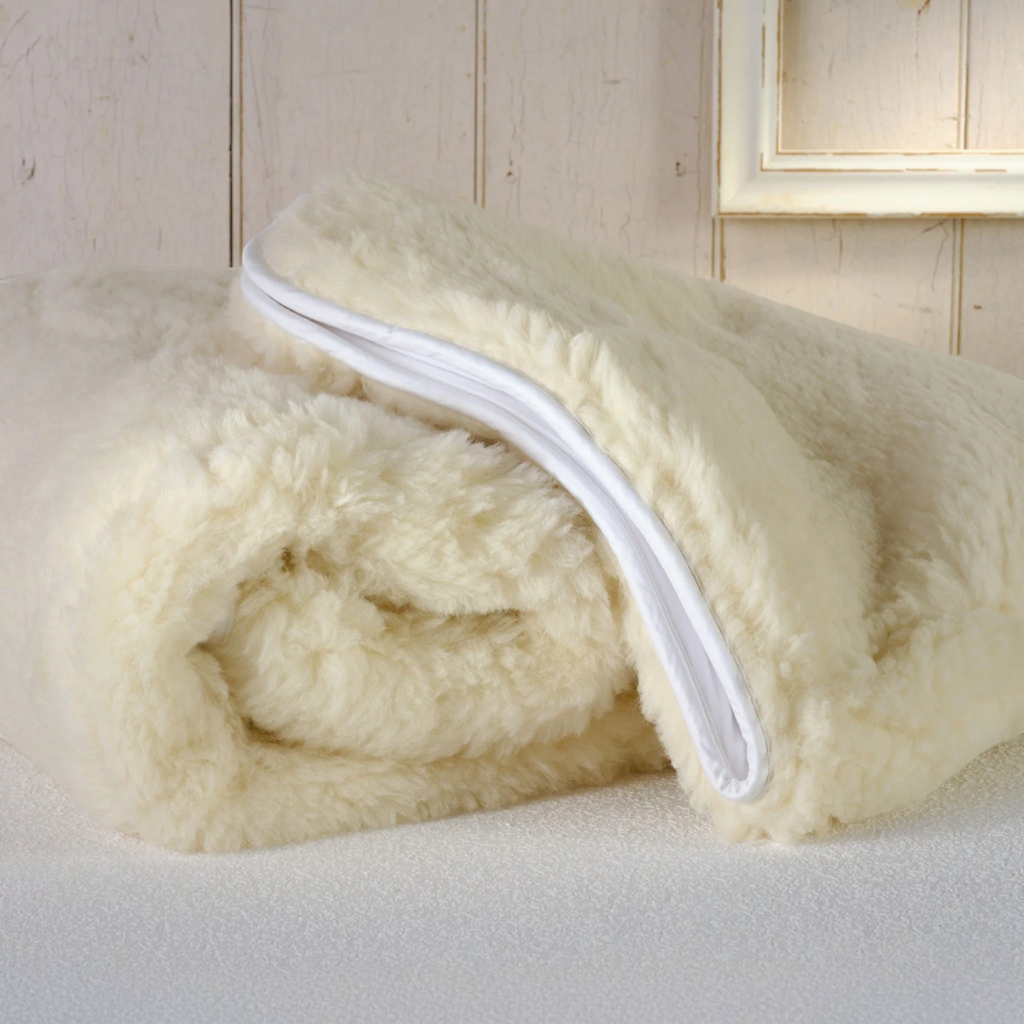 Folded cream-coloured alpaca blanket with a white zipper on a light wooden surface.