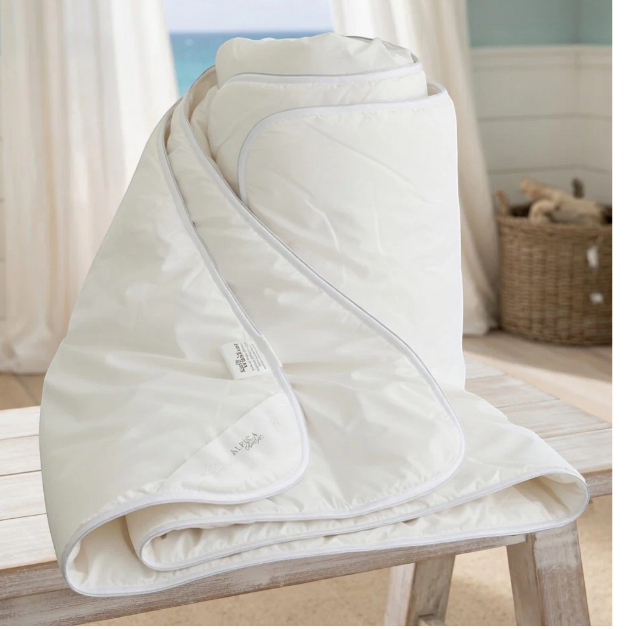 White alpaca quilt draped over a chair with a blurred beach scene in the background
