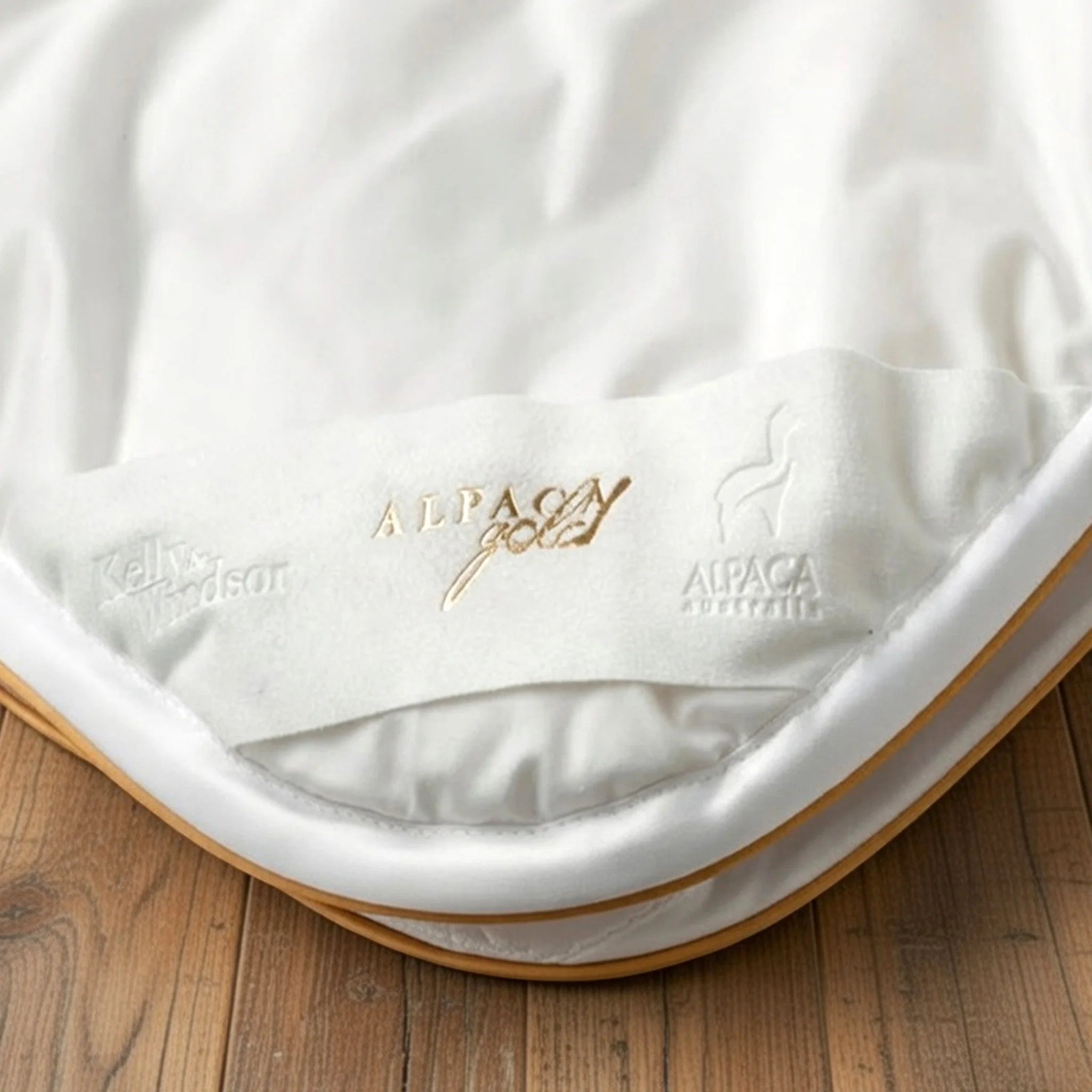 White alpaca blanket with gold branding on a wooden surface
