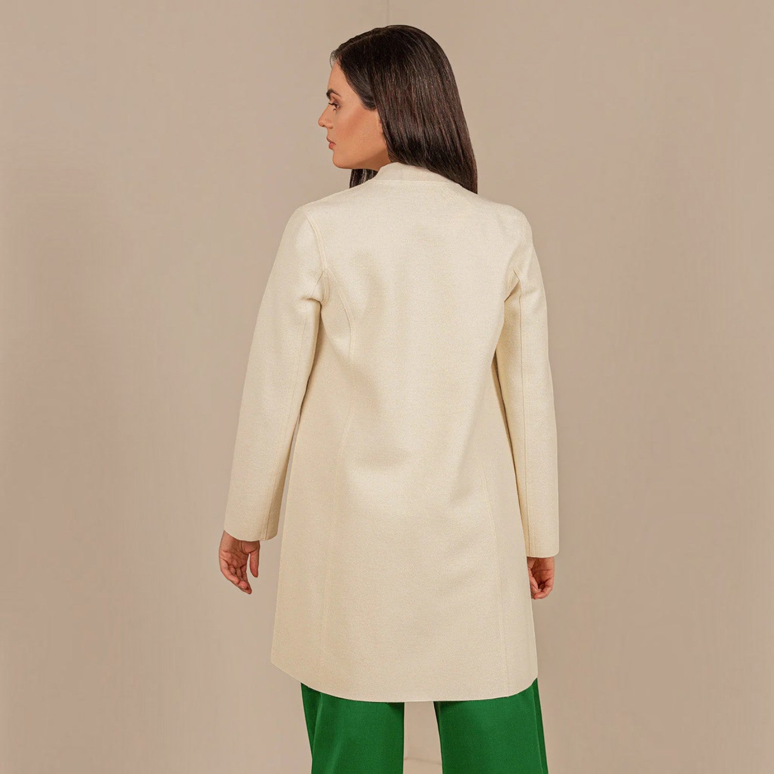 Back view of women’s ecru mid-length alpaca coat styled with green trousers