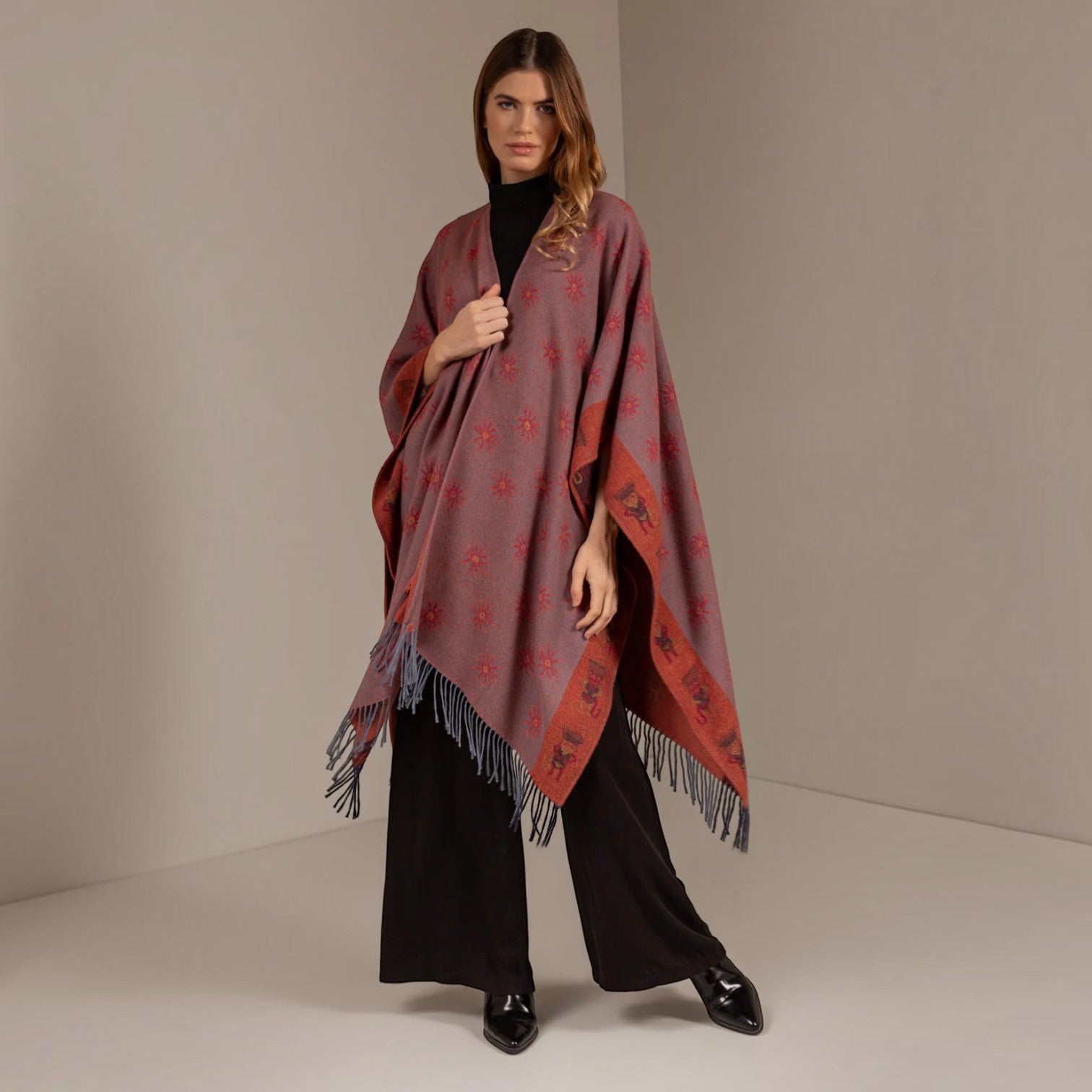 Front view of the terracotta reversible alpaca cape styled with black wide-leg trousers