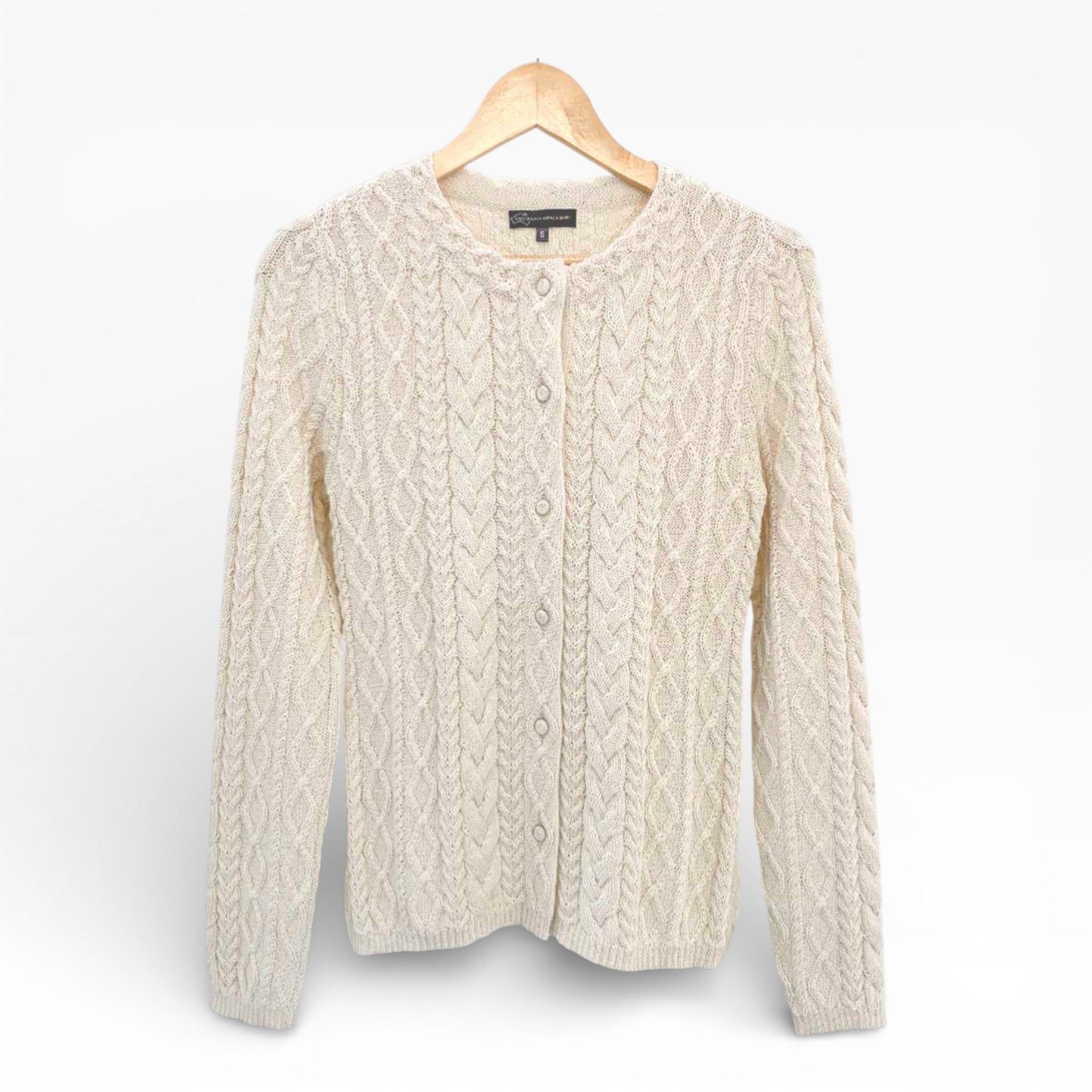 Cream cable knit cardigan on a wooden hanger against a white background