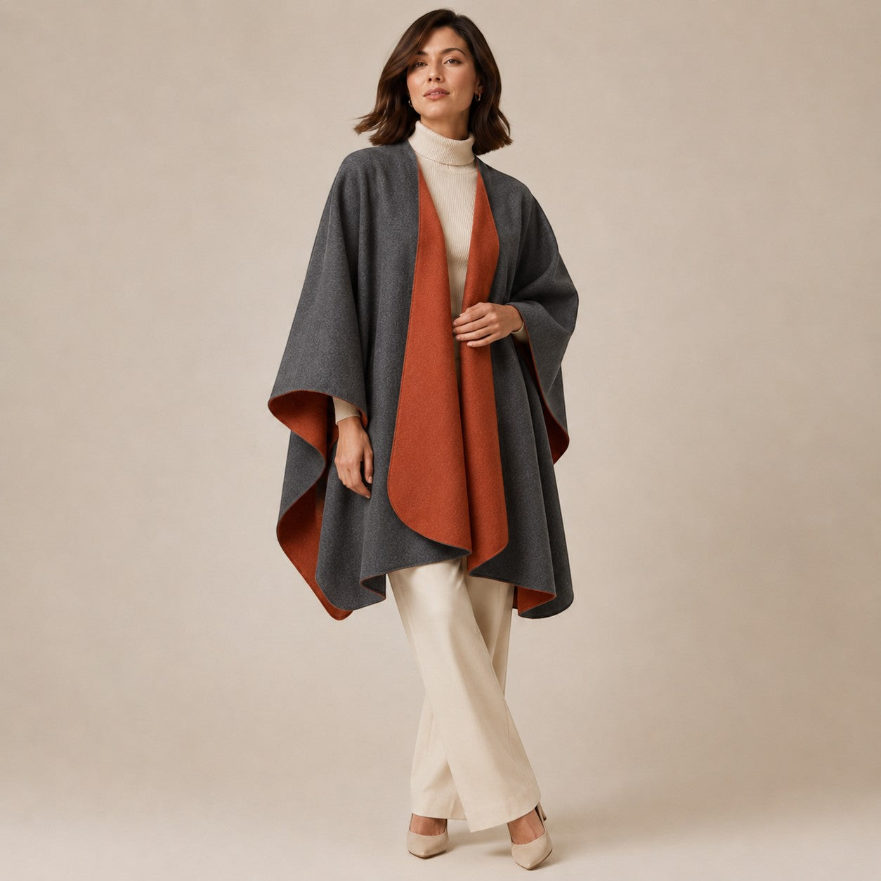 Woman wearing a rust and charcoal reversible alpaca cape over a cream roll-neck sweater.