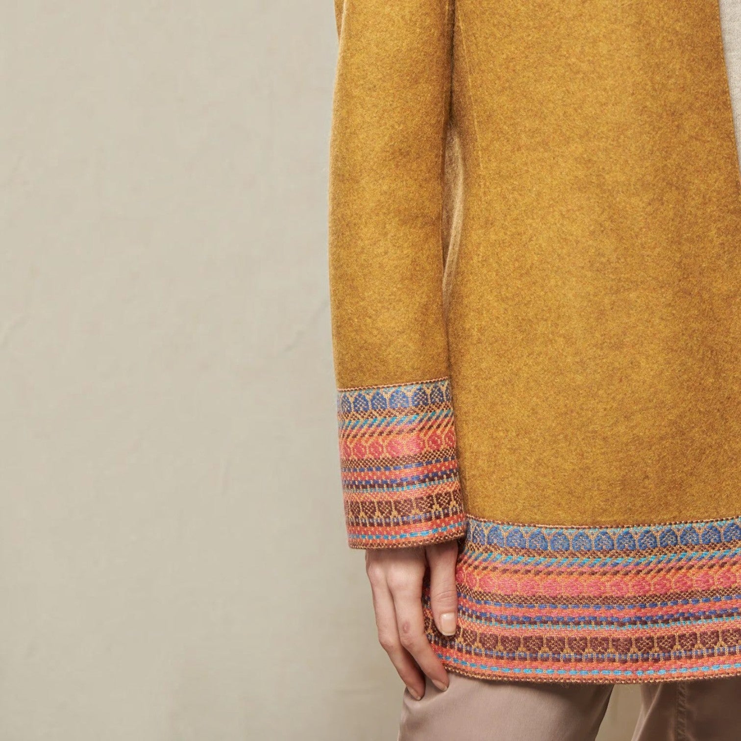 Close-up of the Sangria coat’s mustard alpaca wool fabric and multicoloured patterned trim