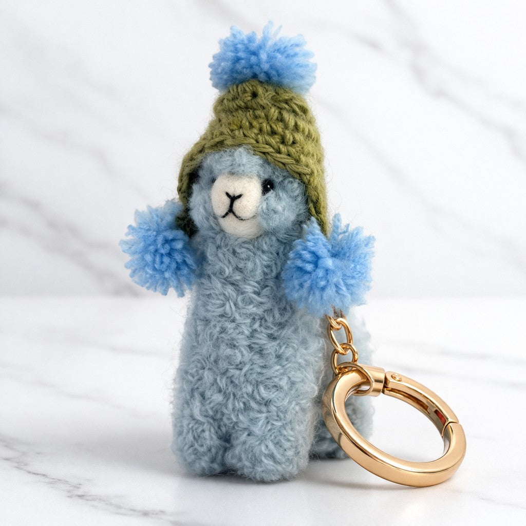 Handmade alpaca keychain with knitted green hat and blue pom-poms