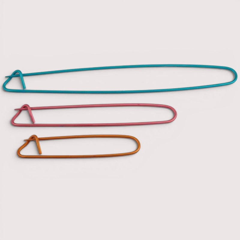 Three colourful knitting stitch holders on a light gray background
