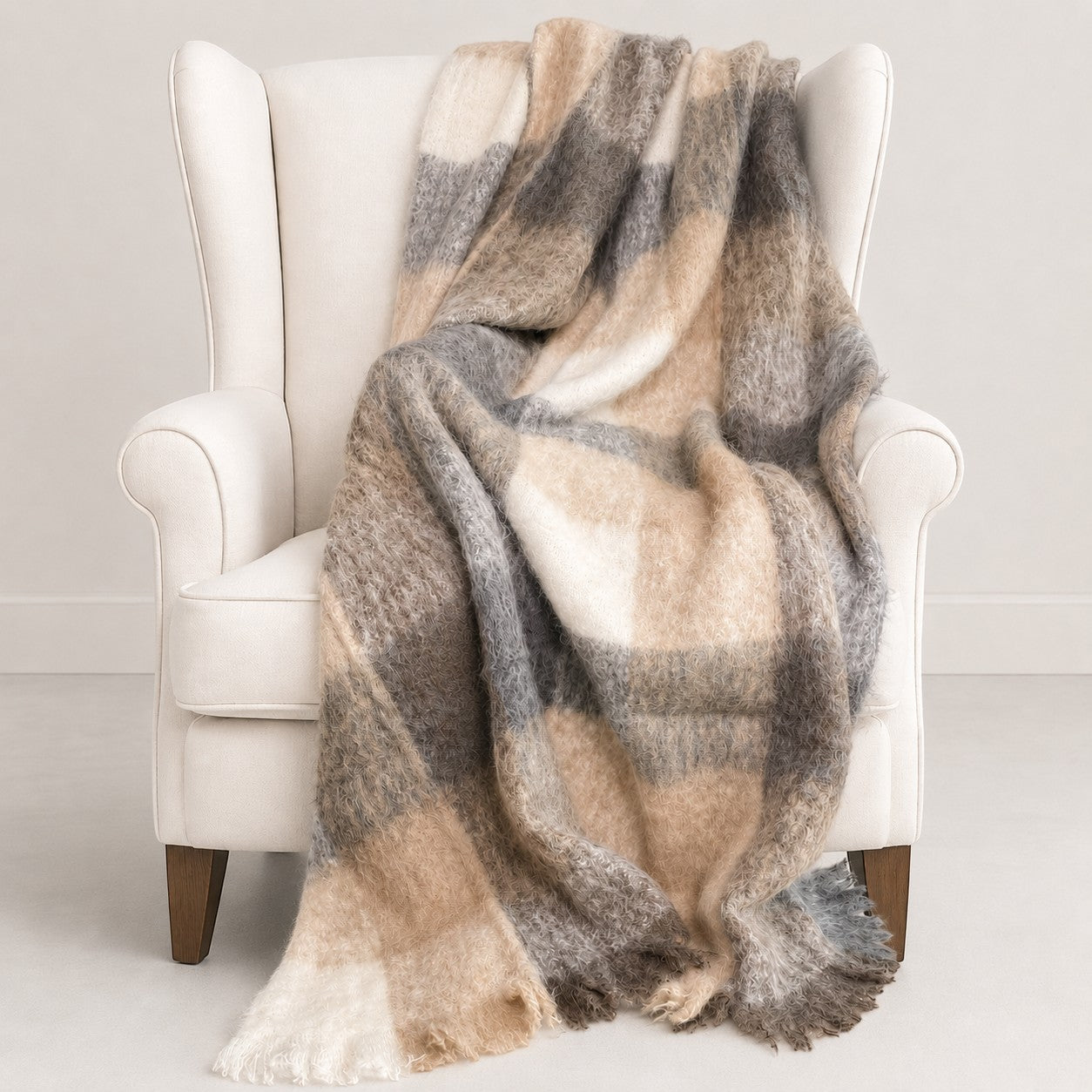 Plaid alpaca blanket draped over a white armchair on a light gray background