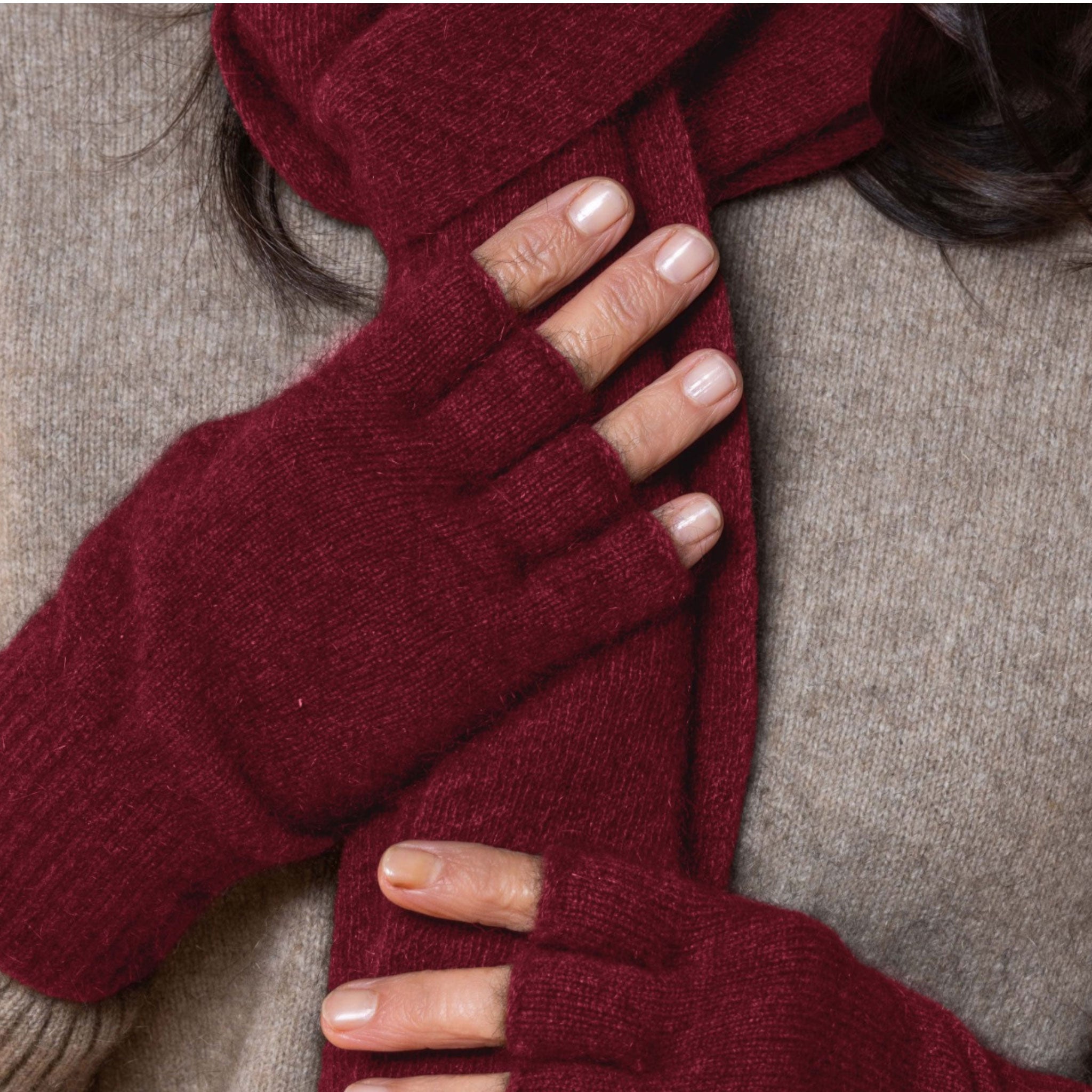 Close-up of a person wearing red fingerless possum gloves on a neutral background