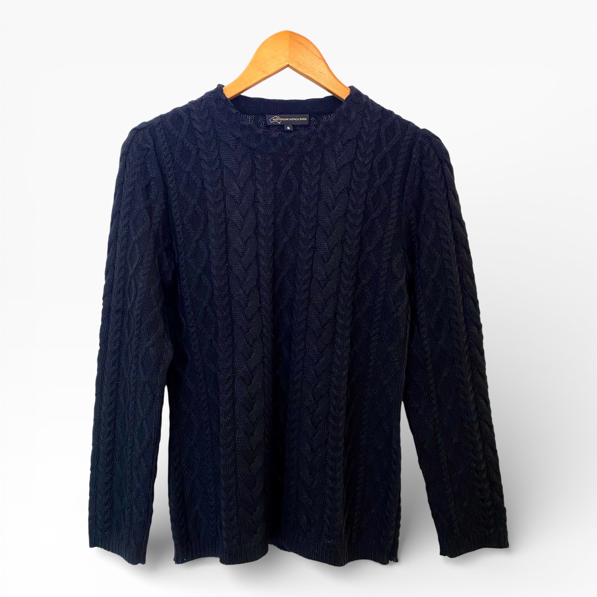 Black cable knit sweater on a wooden hanger against a white background