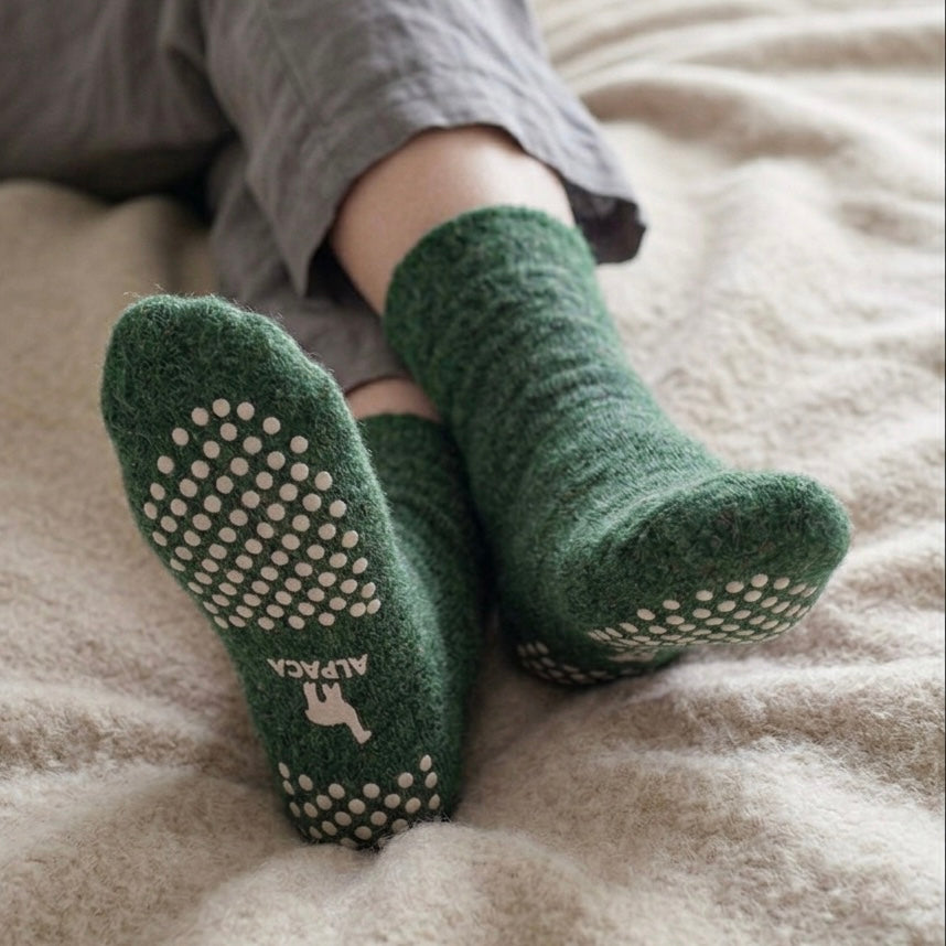 Feet wearing green alpaca slipper socks at home, warm cosy socks with grip soles.