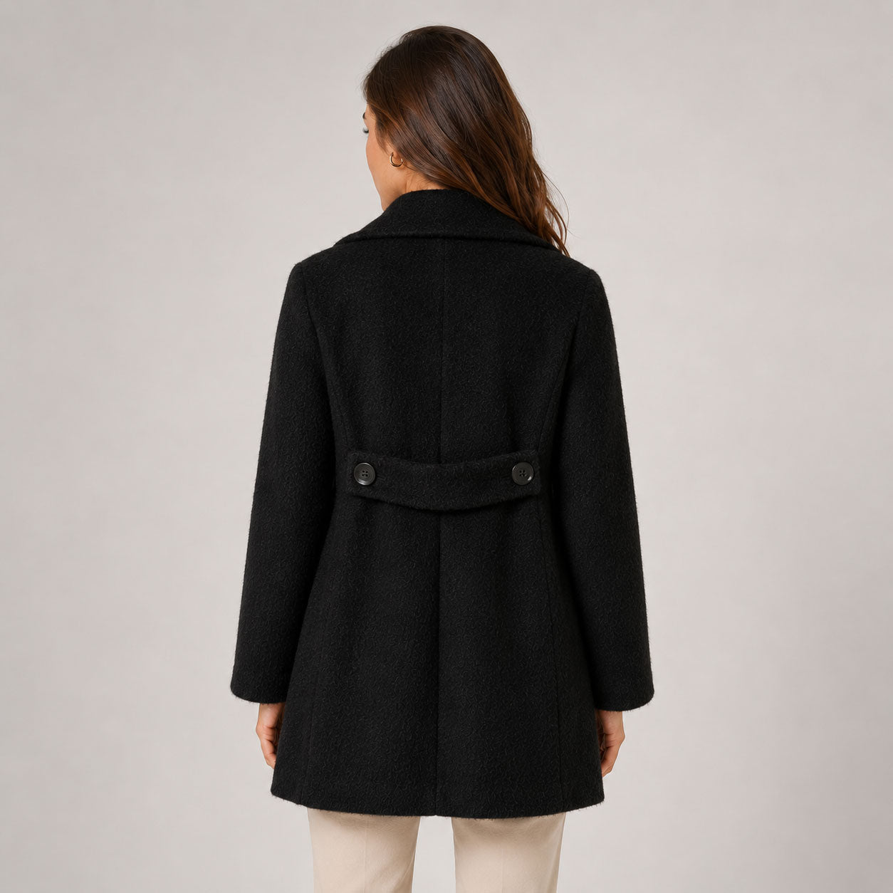Women’s mid-length black alpaca coat styled with cream trousers back view