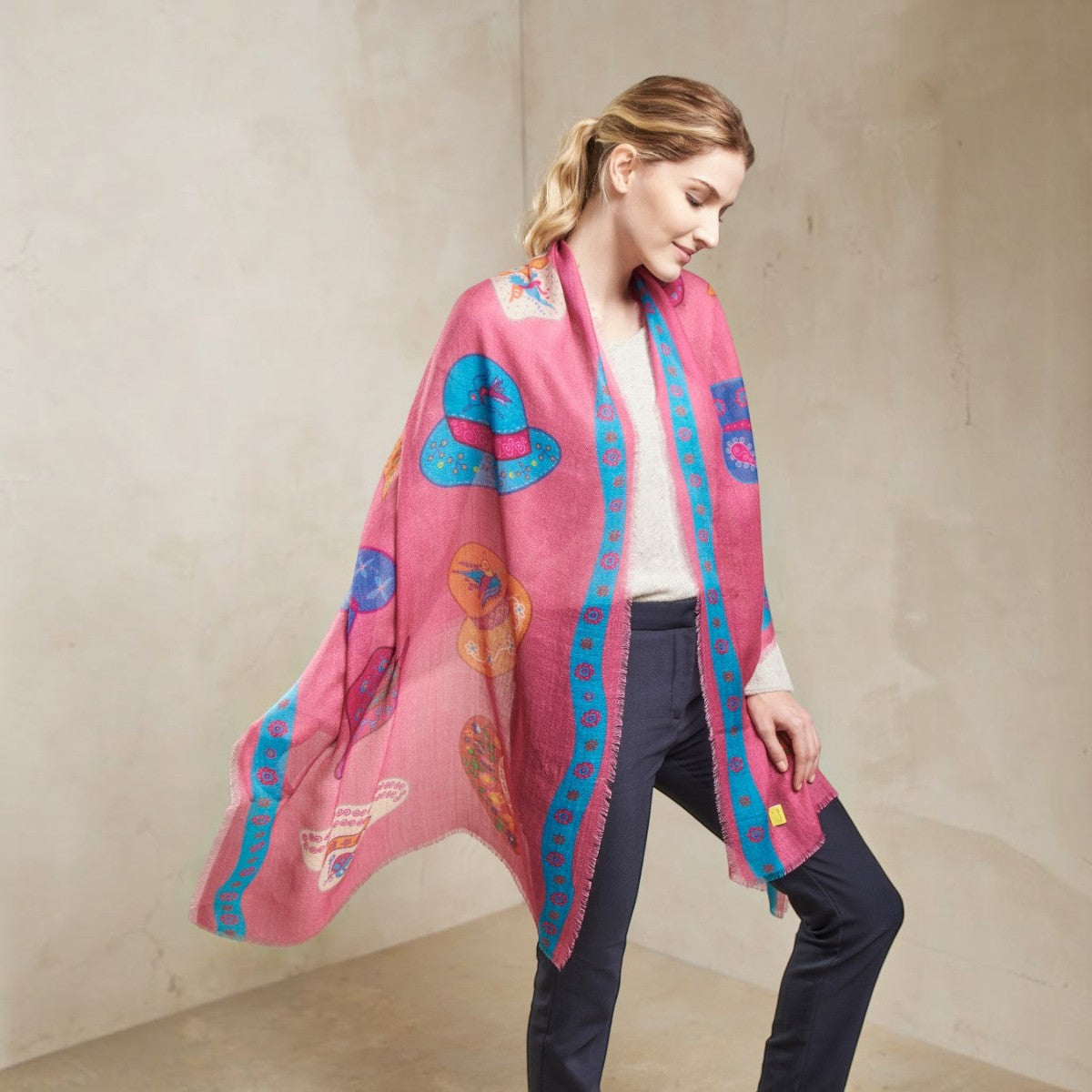 A woman wearing a vibrant pink Alpaca & Silk wrap with colourful illustrations.