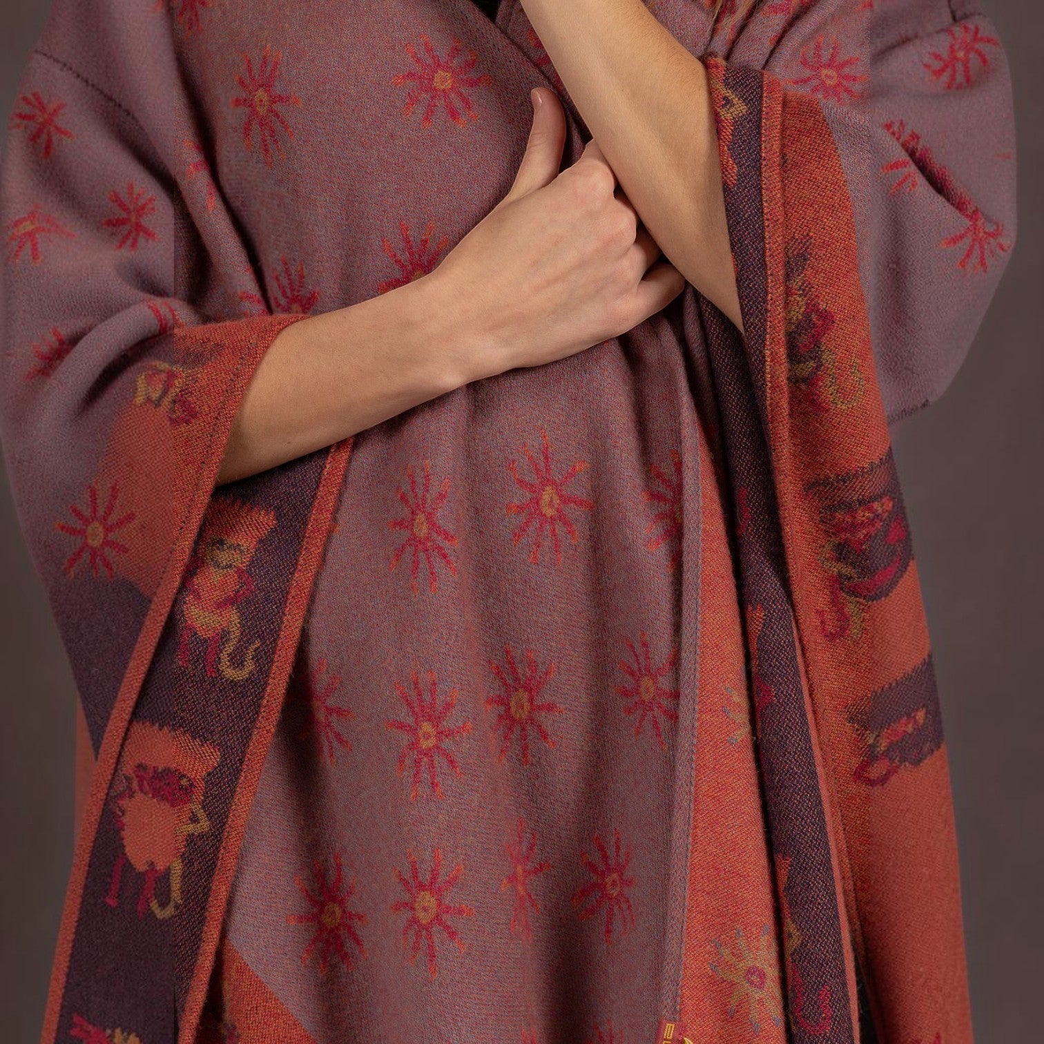 Close-up of the terracotta alpaca cape showing woven sun motifs and decorative border