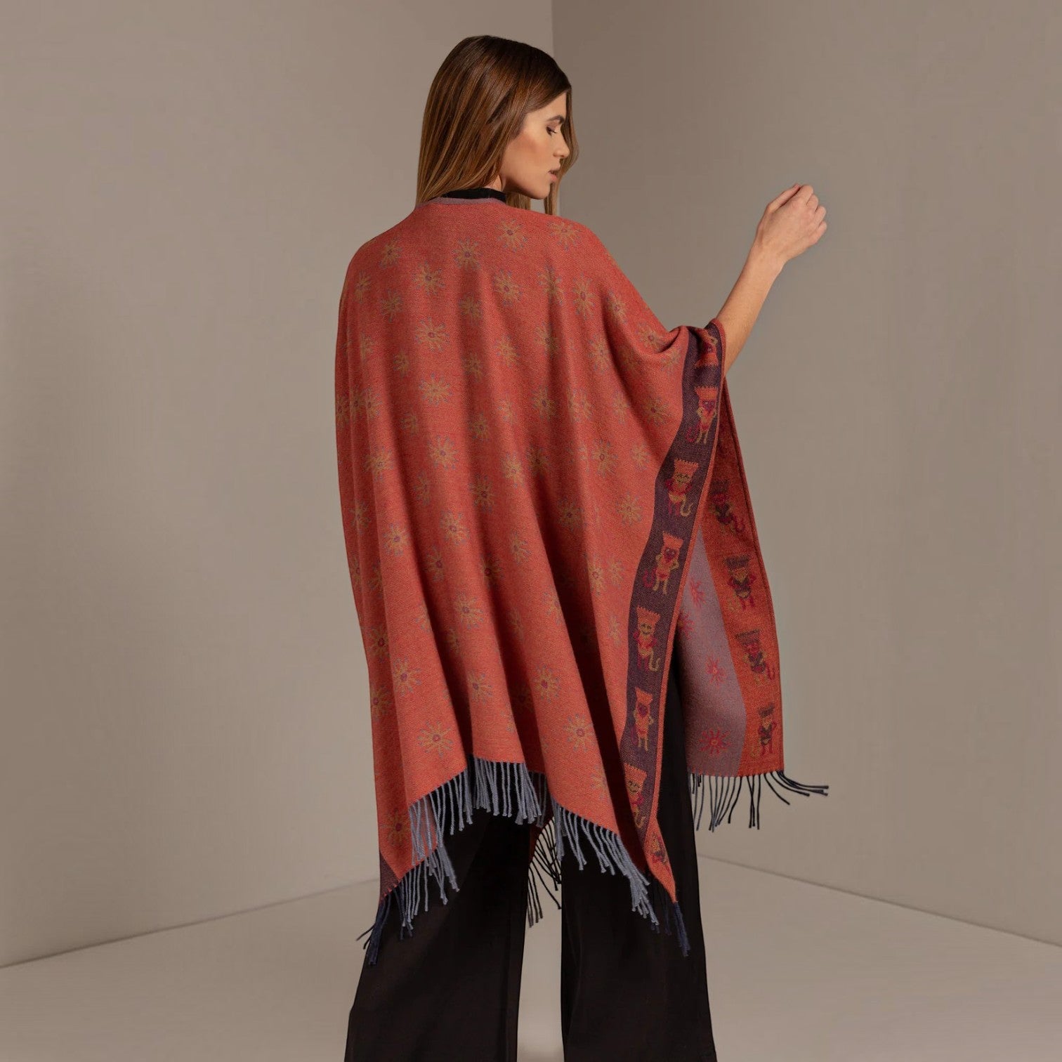 Back view of the Nazca 43 reversible alpaca cape in mauve with red sun motifs and fringed hem