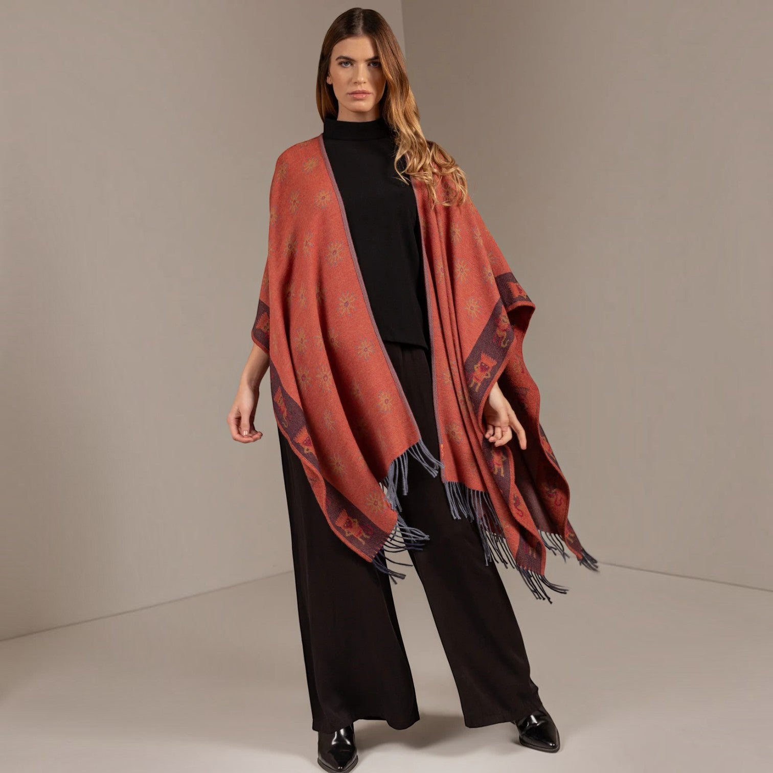 Front view of the terracotta reversible alpaca cape styled with black wide-leg trousers