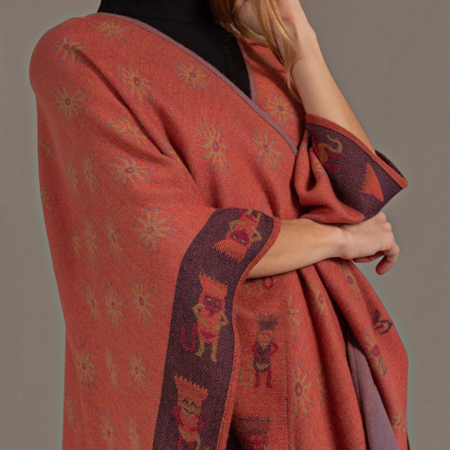 Close-up of the terracotta alpaca cape showing woven sun motifs and decorative border