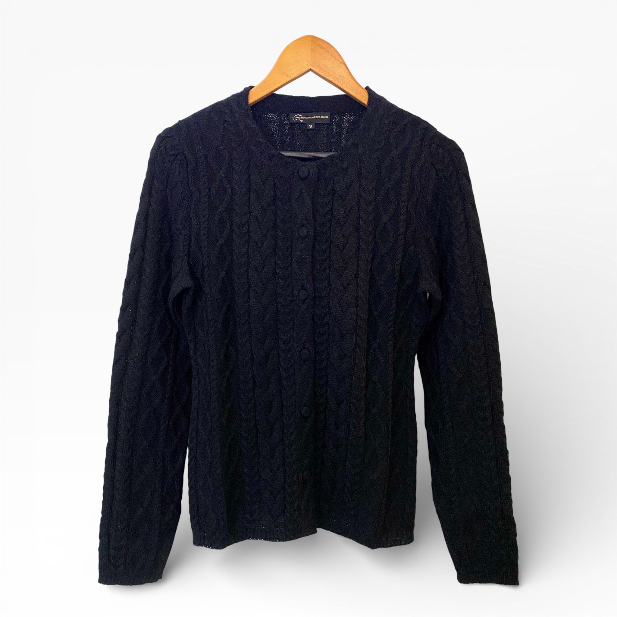 Black cable knit sweater on a wooden hanger against a white background