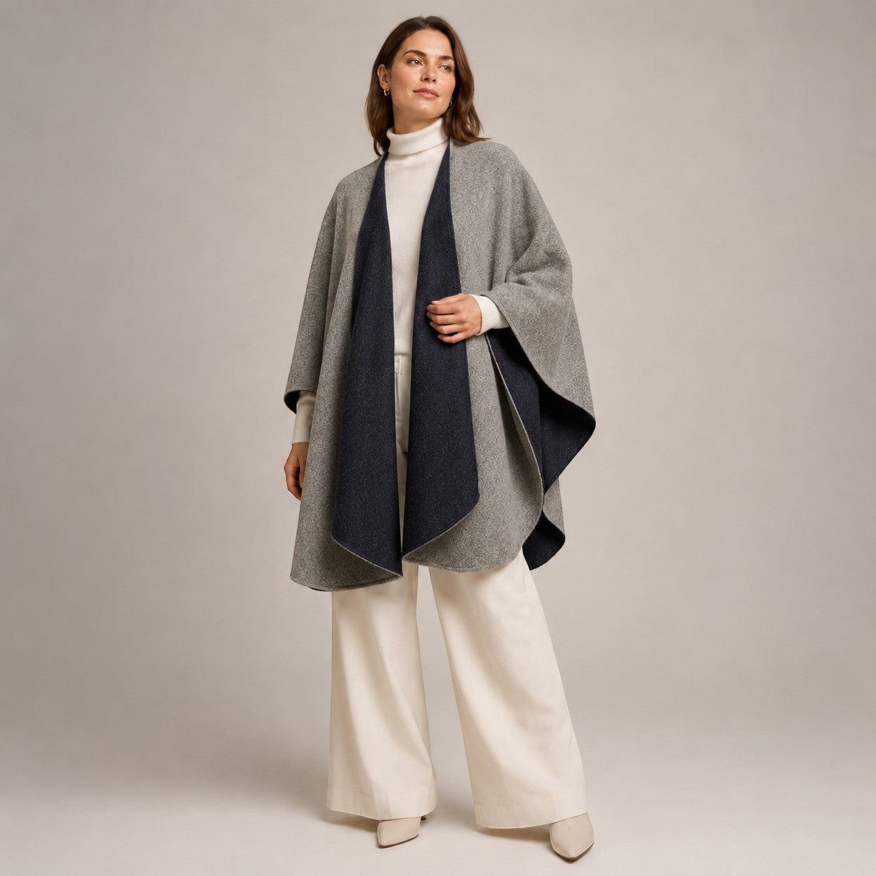 Woman wearing a black and silver reversible alpaca cape over a cream roll-neck sweater.