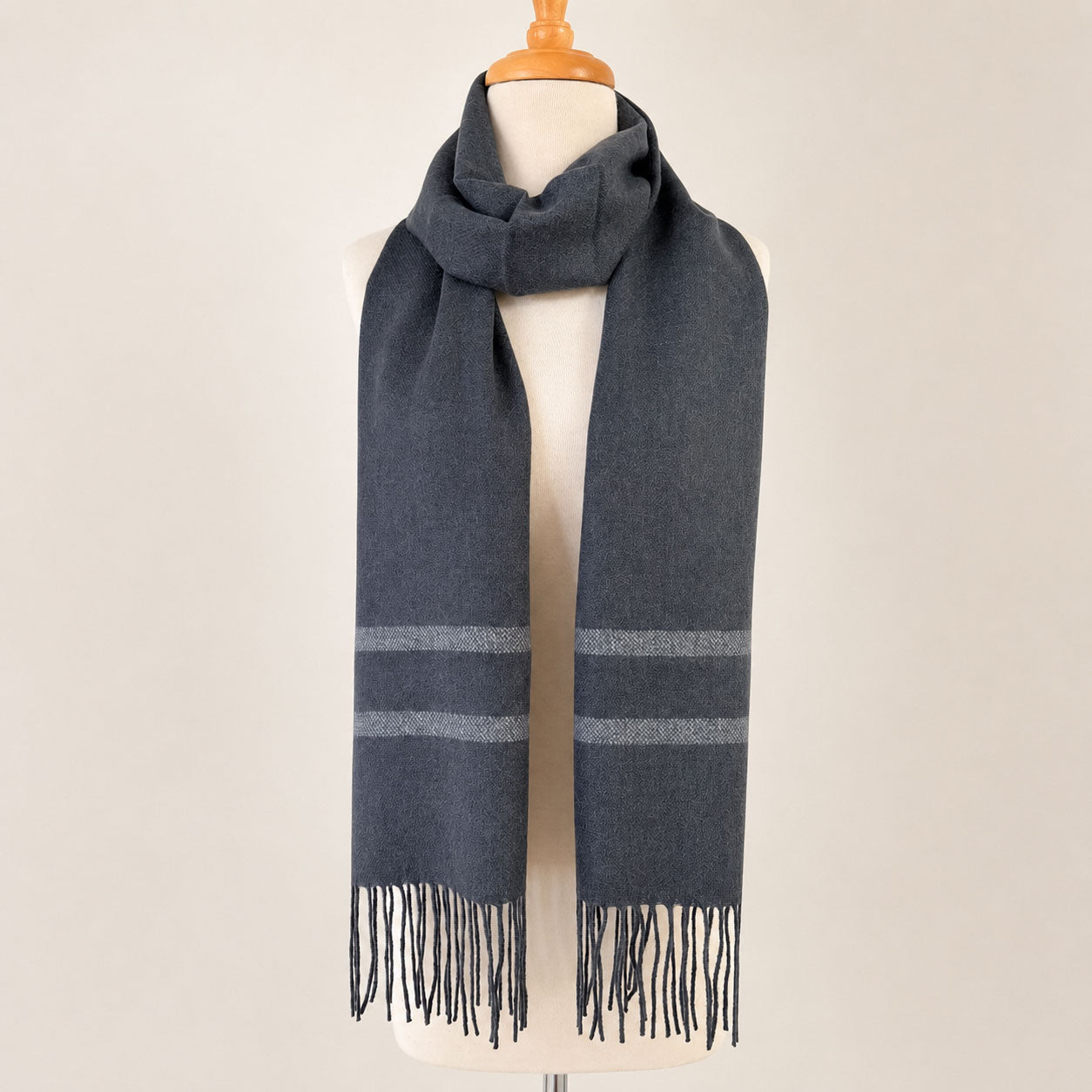 Gray alpaca scarf with striped pattern and fringes on a mannequin against a beige background 