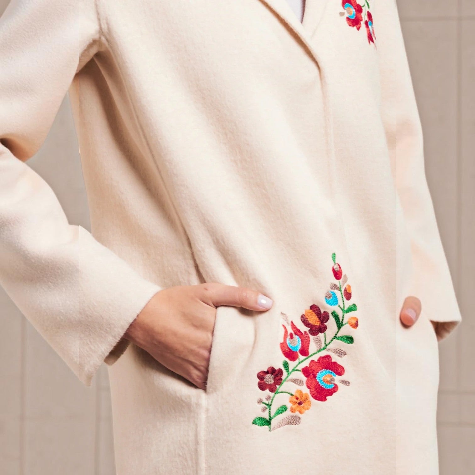 Close-up of colourful floral embroidery on the pocket of the Selina cream alpaca coat