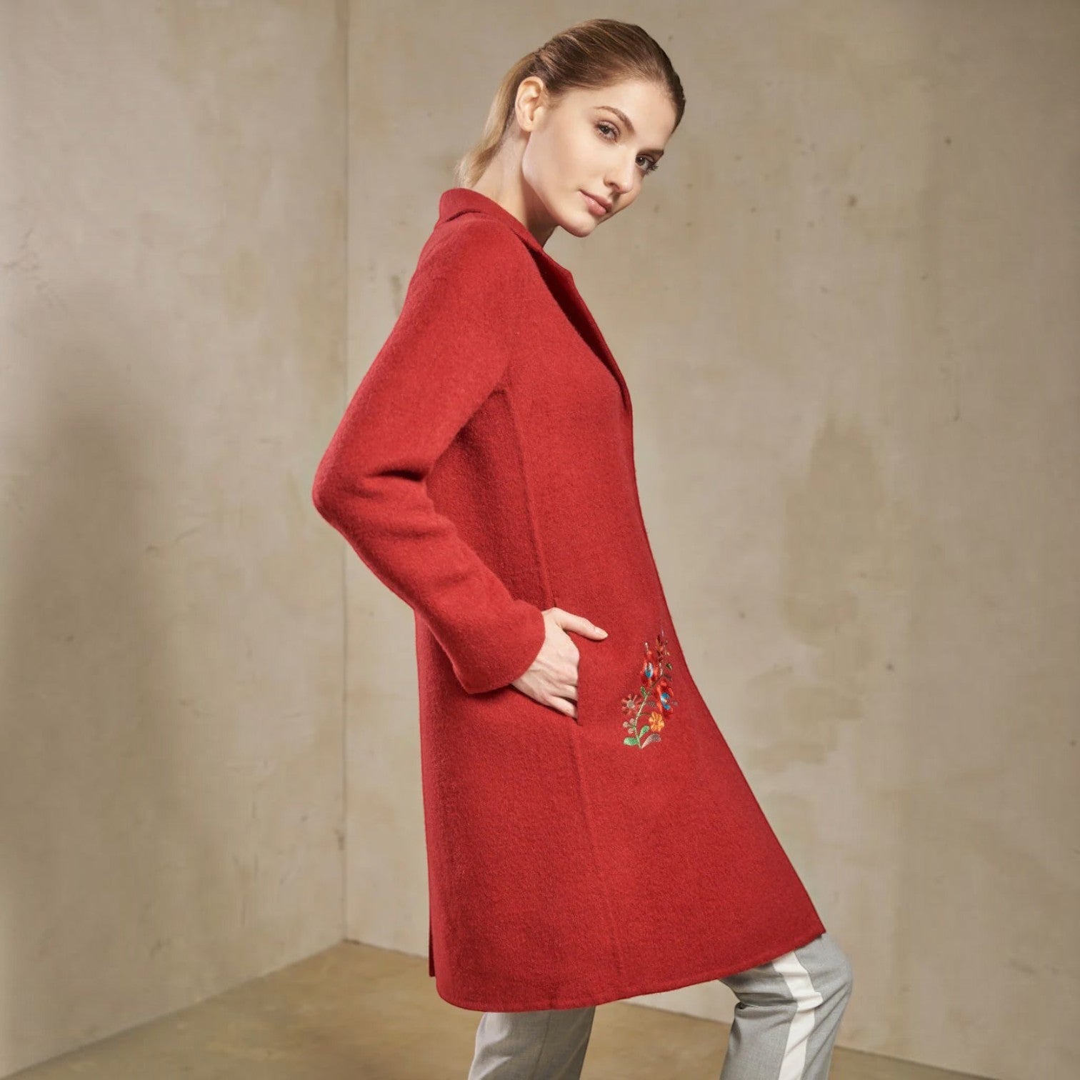 Side view of the Selina ruby red alpaca coat showing its relaxed fit and embroidered pocket detail
