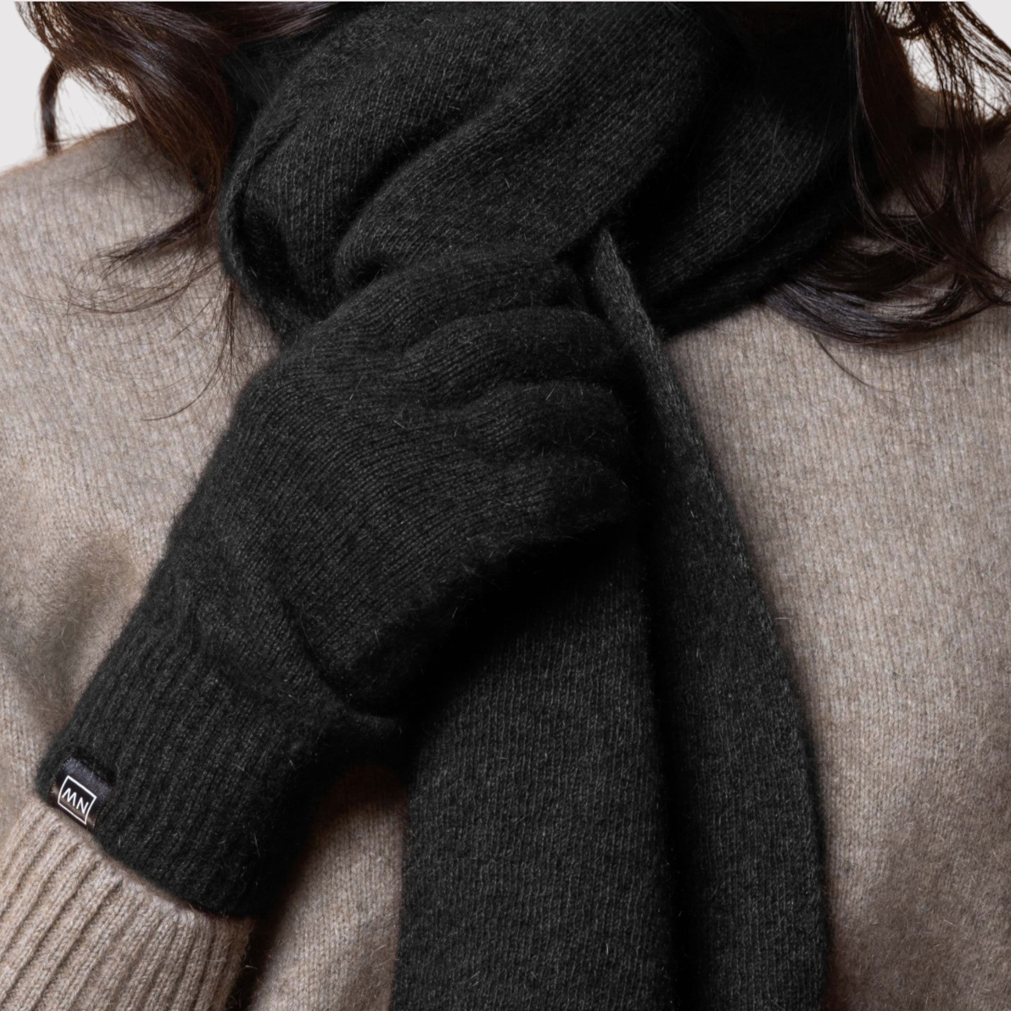 Person wearing a dark gray possum scarf with a brand label on a neutral background