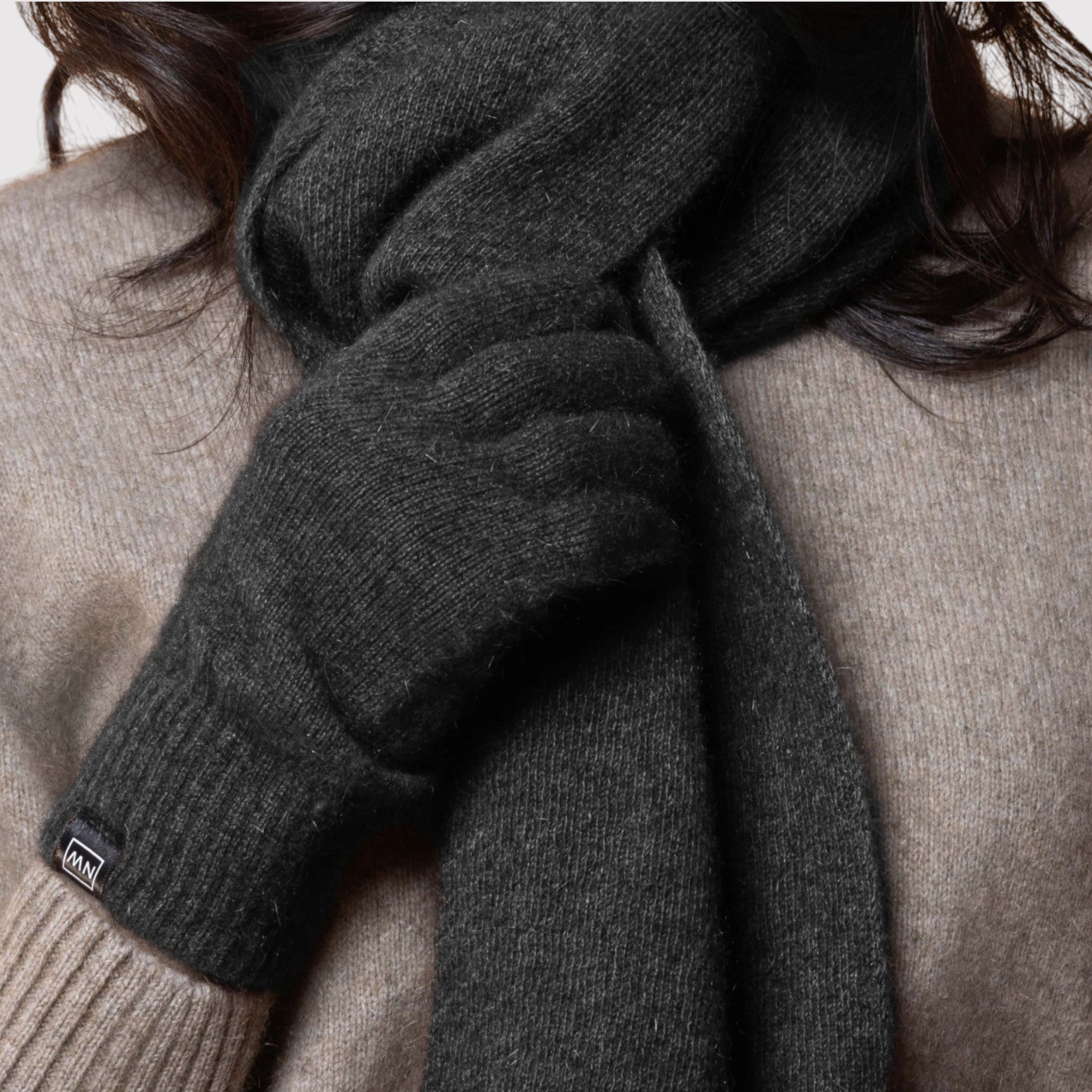 Person wearing a dark gray possum scarf and gloves with a brand logo, against a neutral background