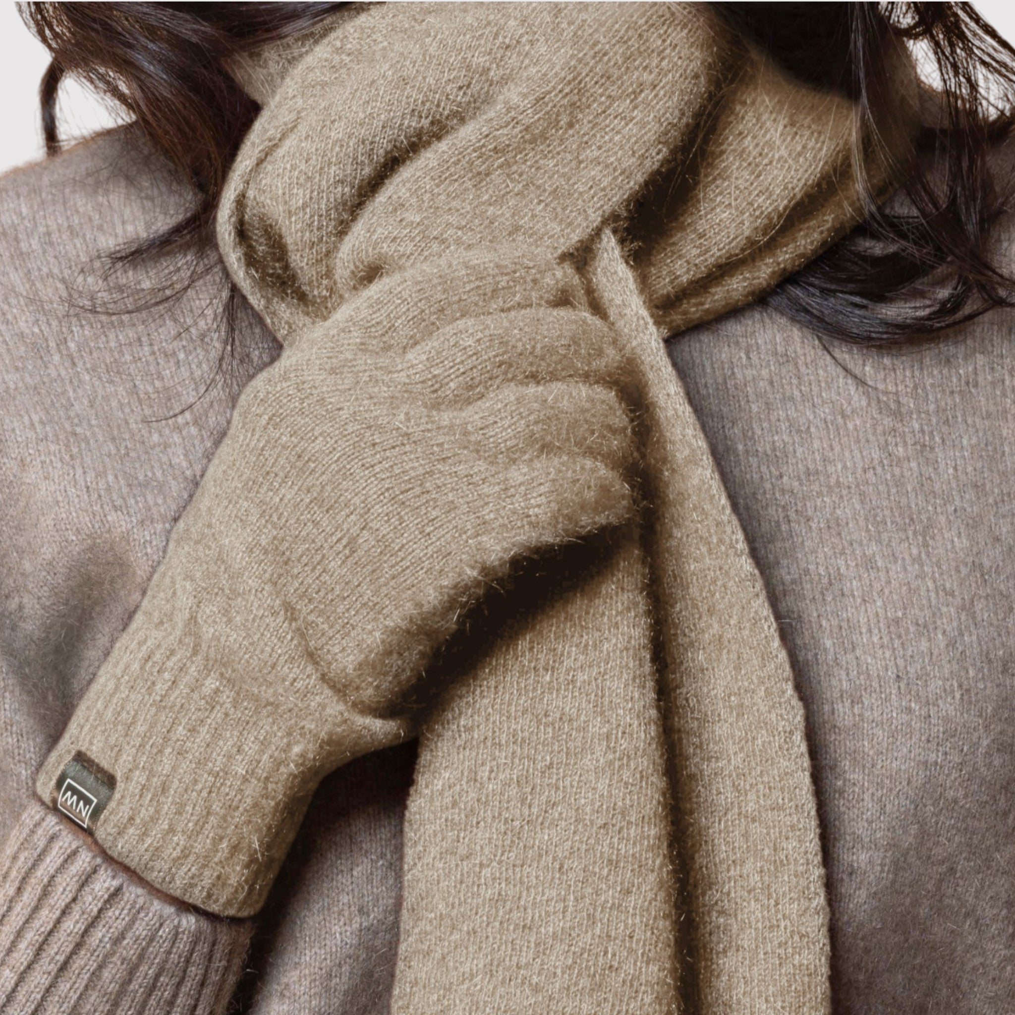 Close-up of a person wearing a beige possum scarf with a brand label, against a neutral background.