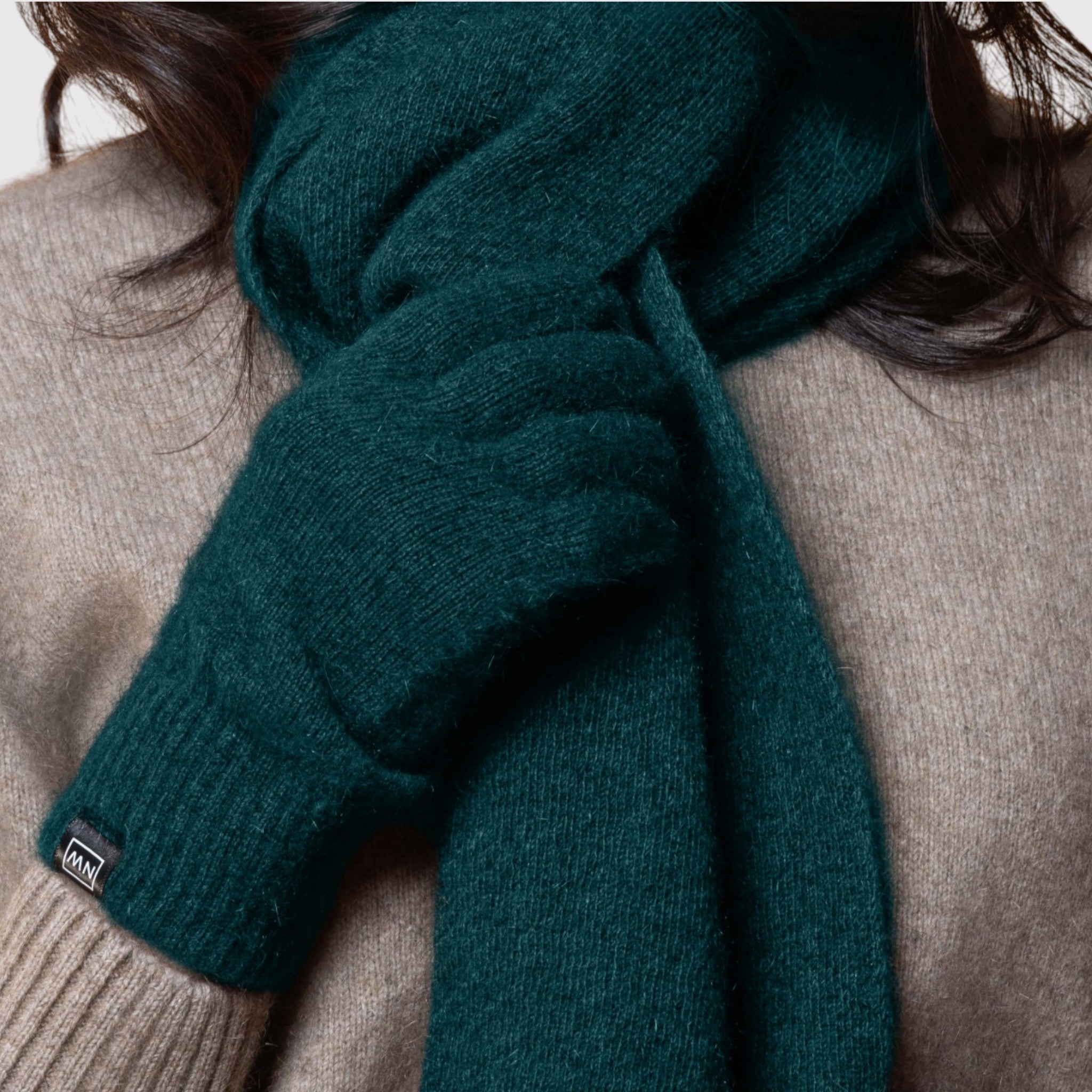 Person wearing a green possum scarf and gloves with a beige background