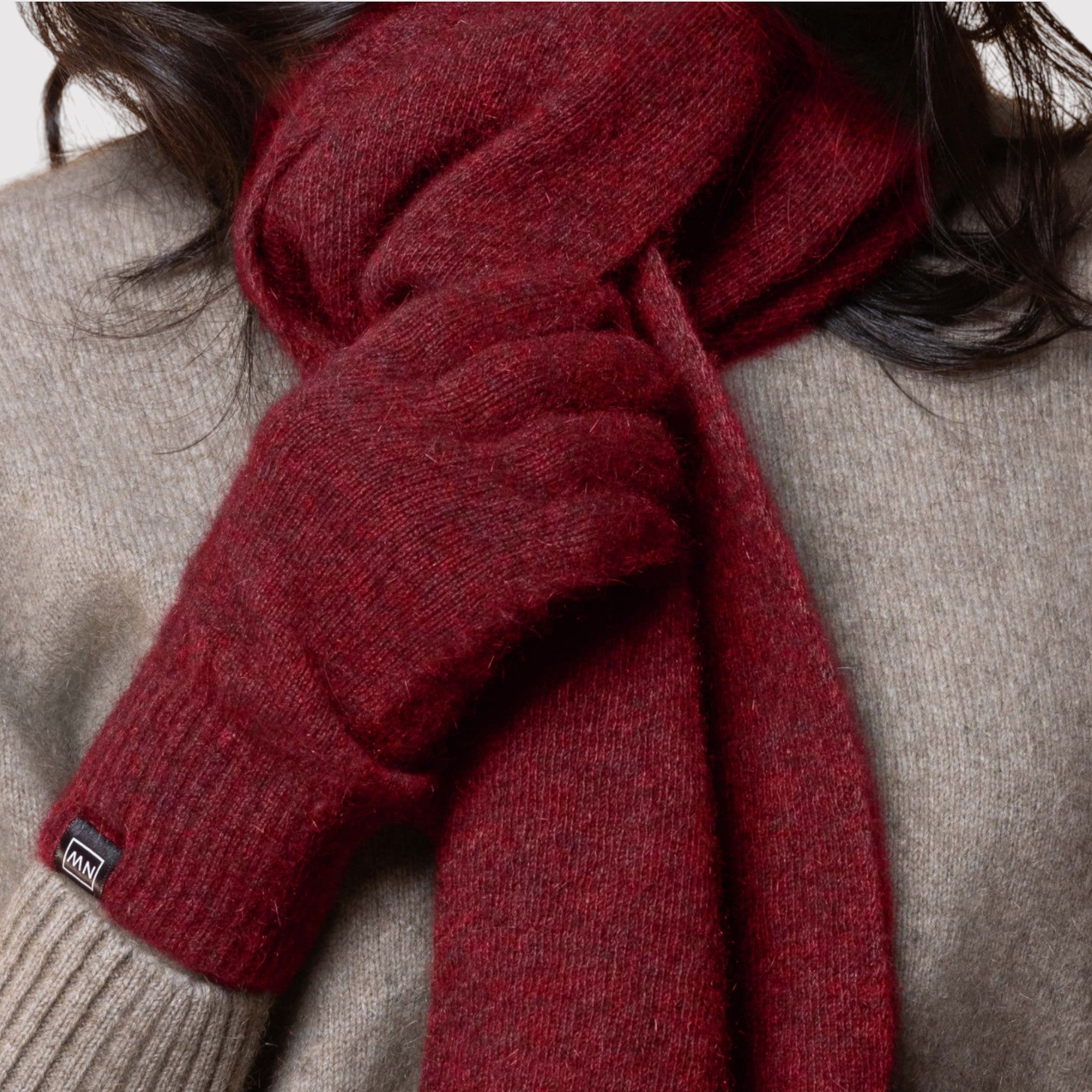 Red possum scarf with a brand label worn by a person in a gray sweater.