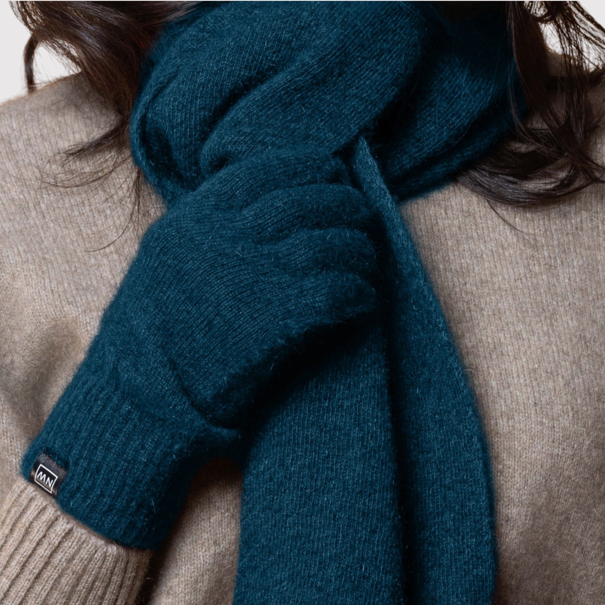 Person wearing a blue possum scarf and gloves with a beige background