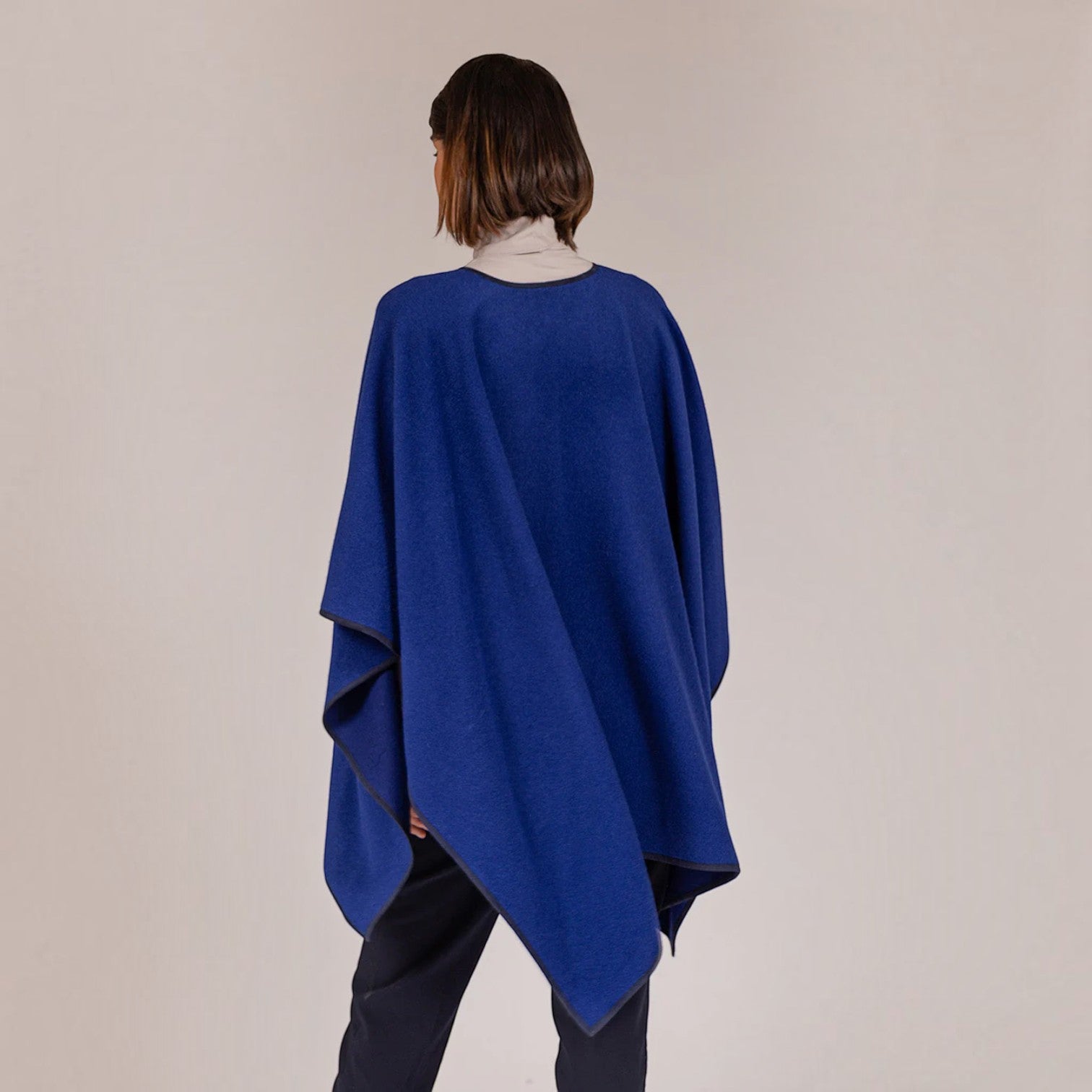 Back view of royal blue alpaca cape with draped silhouette and dark trim