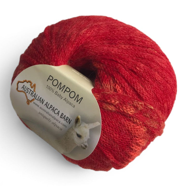 Doughnut of 100% Baby Alpaca PomPom Yarn in variegated red, crimson and coral tones.